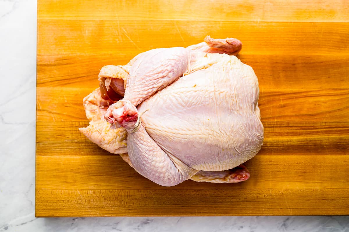 A chicken is sitting on a wooden cutting board.