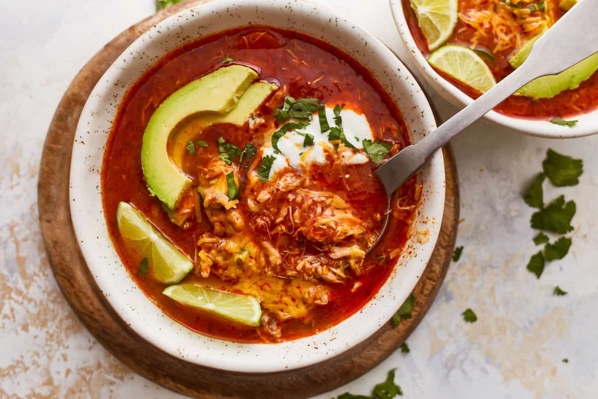 Two bowls of mexican chicken soup with avocado and lime.