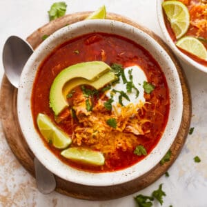 Two bowls of mexican chicken soup with sour cream and avocado.