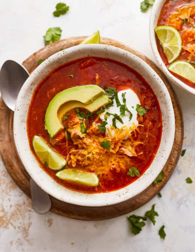 Two bowls of mexican chicken soup with sour cream and avocado.