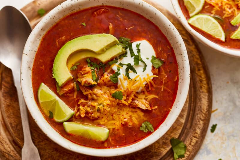 Two bowls of mexican chicken soup on a wooden board.