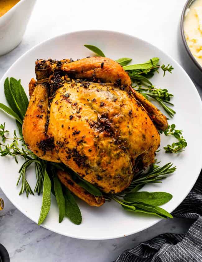 Roasted chicken on a plate with gravy and sprigs of thyme.