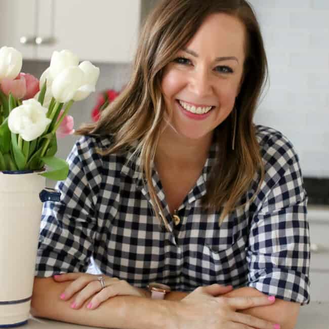 headshot of Becky Hardin A woman in a plaid shirt is smiling in front of a vase of flowers.