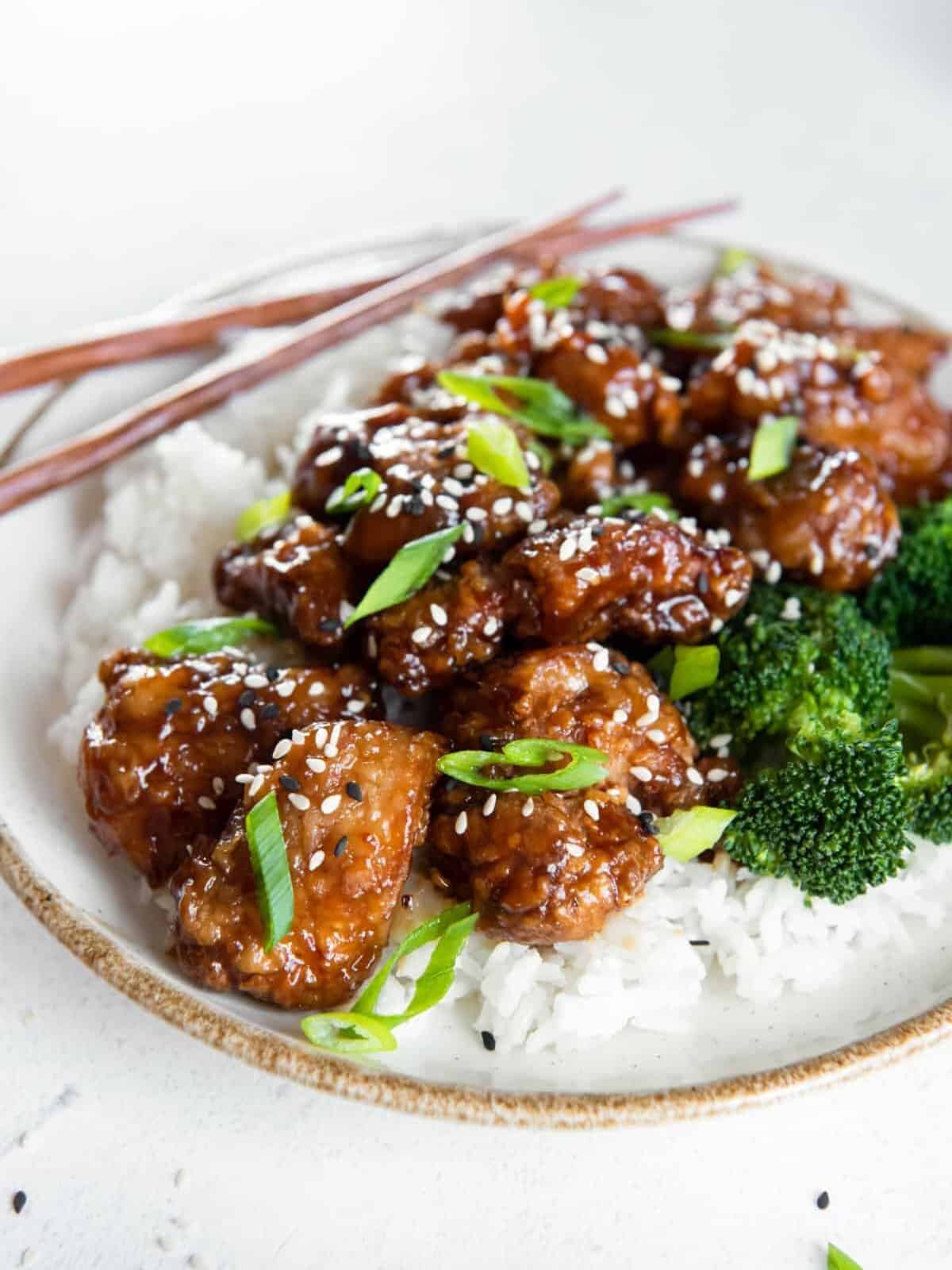 a plate of general tsos chicken with chopsticks.