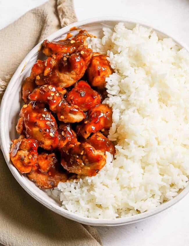 A bowl of rice with General Tso's chicken and sauce on it.