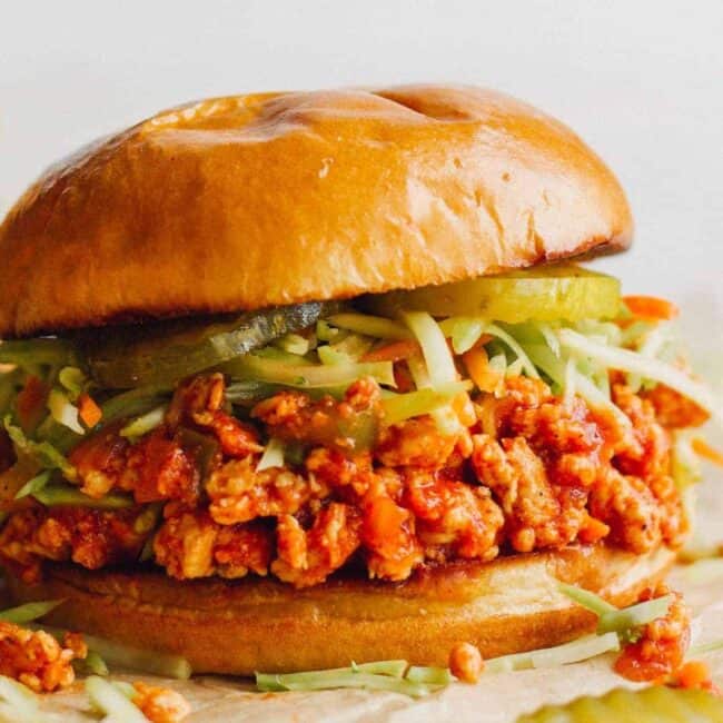 up close image of chicken sloppy joes topped with slaw and pickles