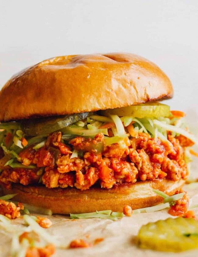 up close image of chicken sloppy joes topped with slaw and pickles