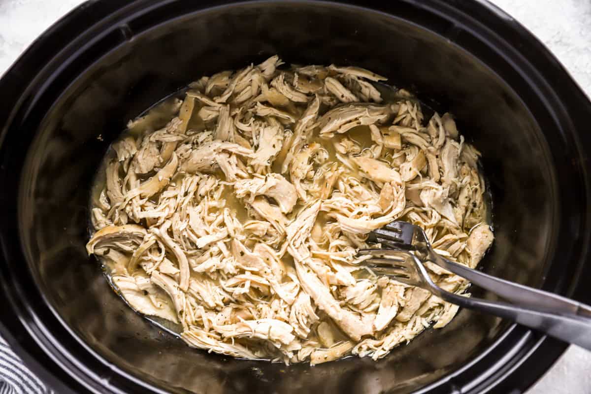 shredded chicken in a slow cooker with 2 forks.