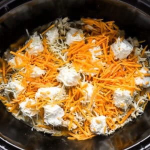 shredded cheese and cream cheese over shredded chicken in a crockpot.