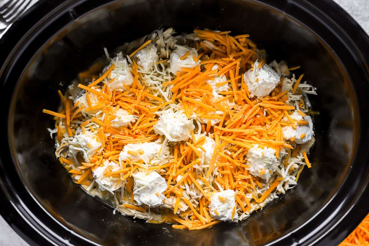 shredded cheese and cream cheese over shredded chicken in a crockpot.