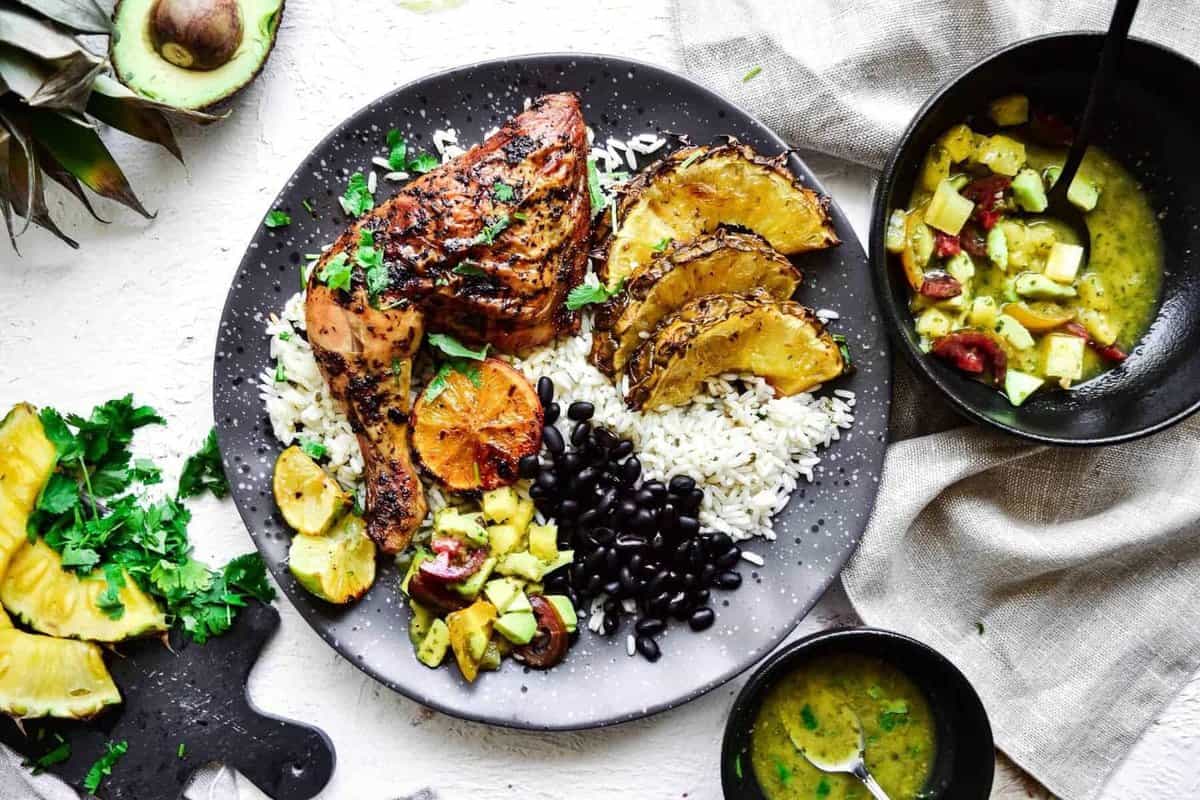 overhead view of cuban chicken on a plate with rice, beans, plantains, and pineapple avocado salsa