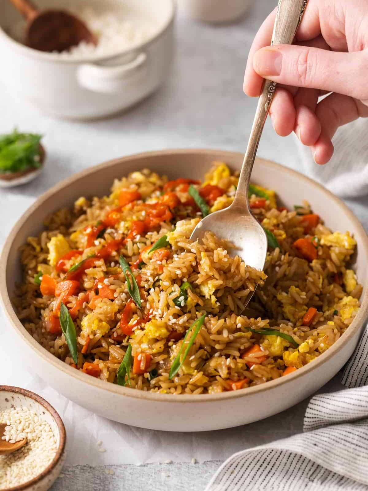three-quarters view of a spoon scooping fried rice with egg and veggies from a white bowl.