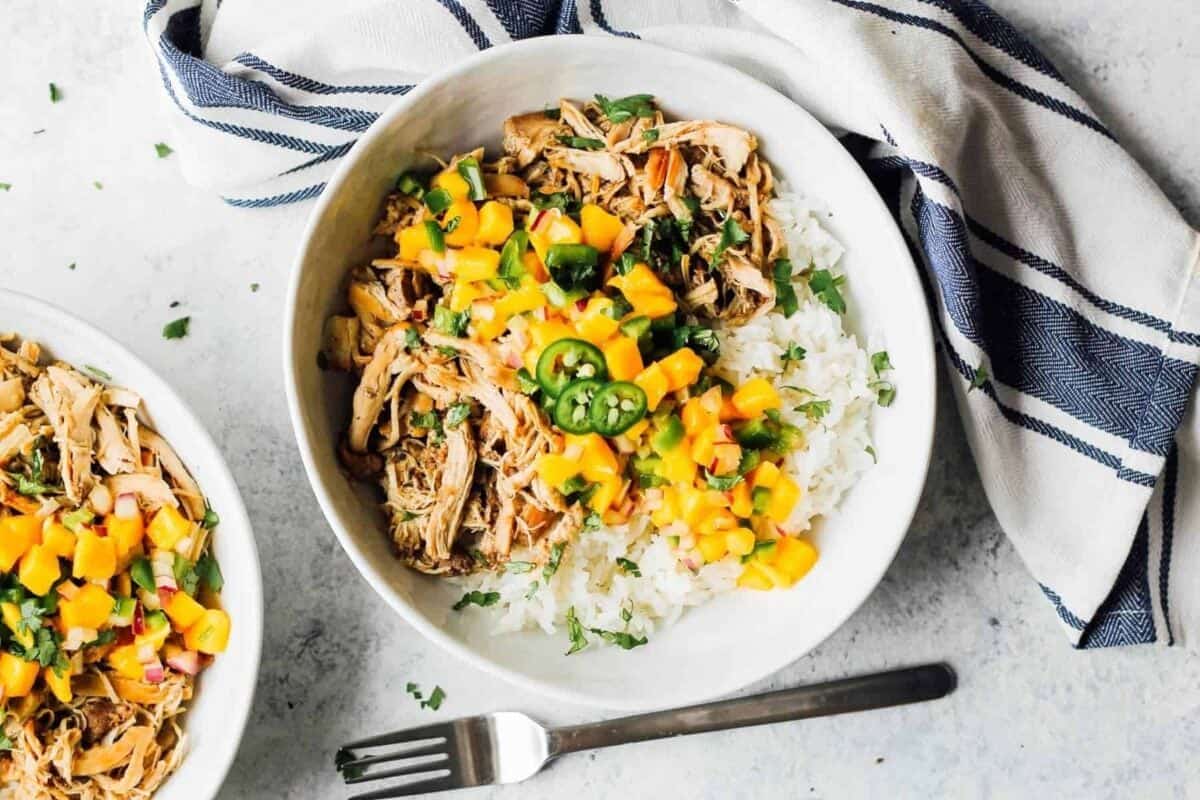 Instant Pot jerk chicken with two bowls of rice and mangoes.