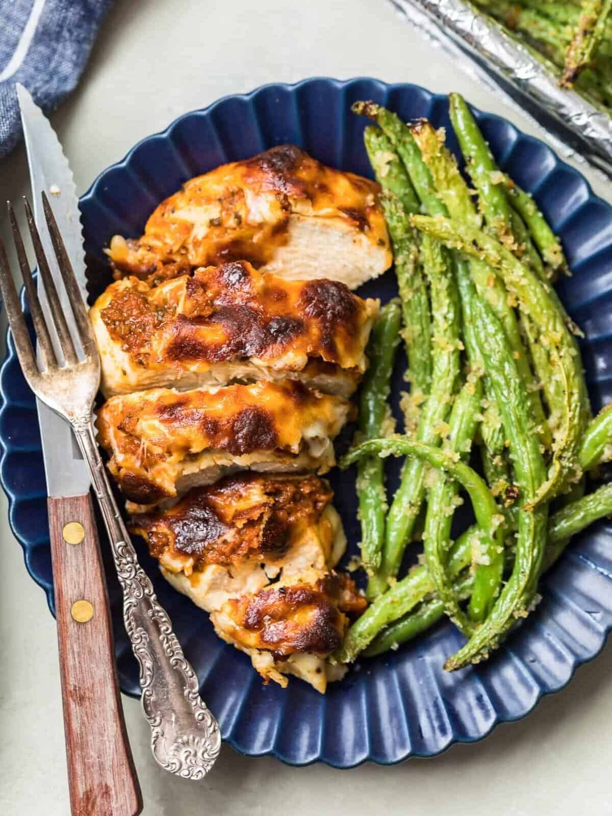 Pesto Mozzarella Chicken and green beans served on a plate with a knife and fork