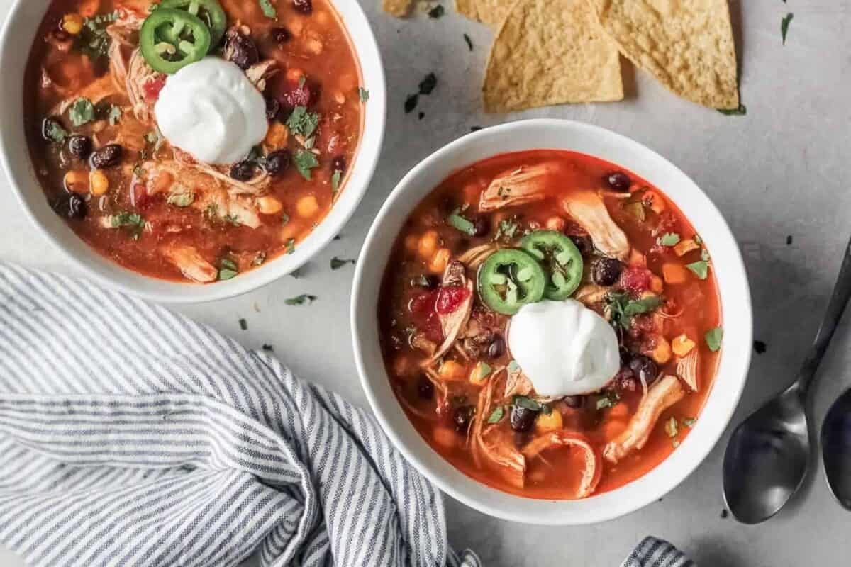 Two bowls of Chicken Enchilada Soup with tortillas and sour cream.