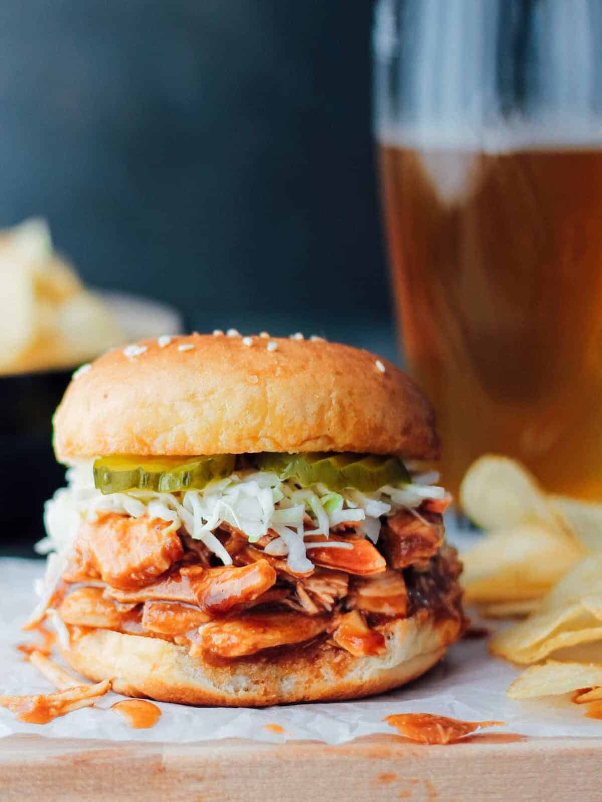 a crockpot bbq chicken sandwich with a glass of beer.