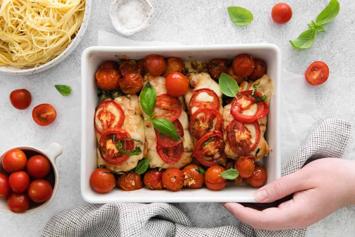 baking dish filled with caprese chicken next to a bowl of pasta
