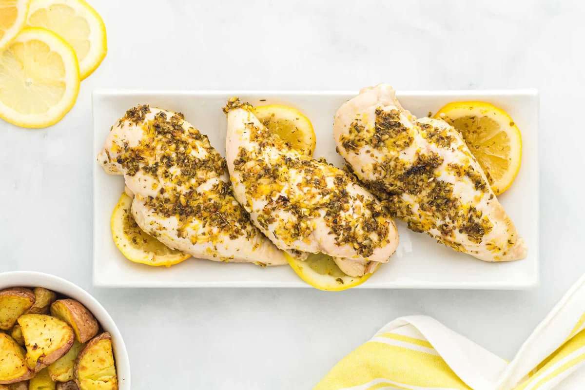 overhead view of baked lemon butter chicken breasts on a white rectangular serving tray.
