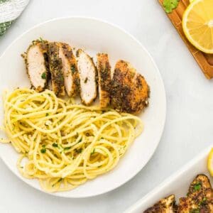 sliced lemon pepper chicken breast with pasta on a white plate.