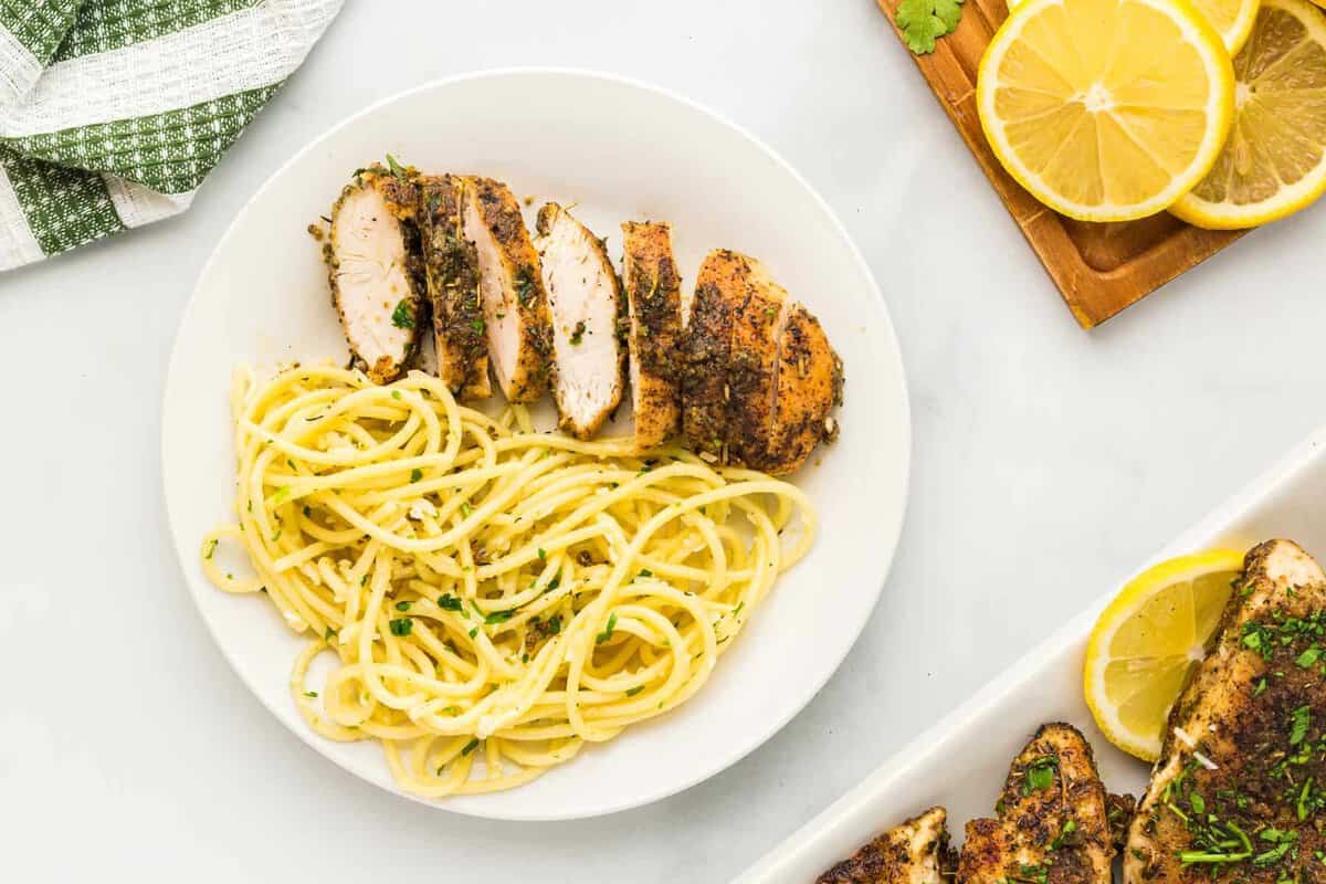 sliced lemon pepper chicken breast with pasta on a white plate.