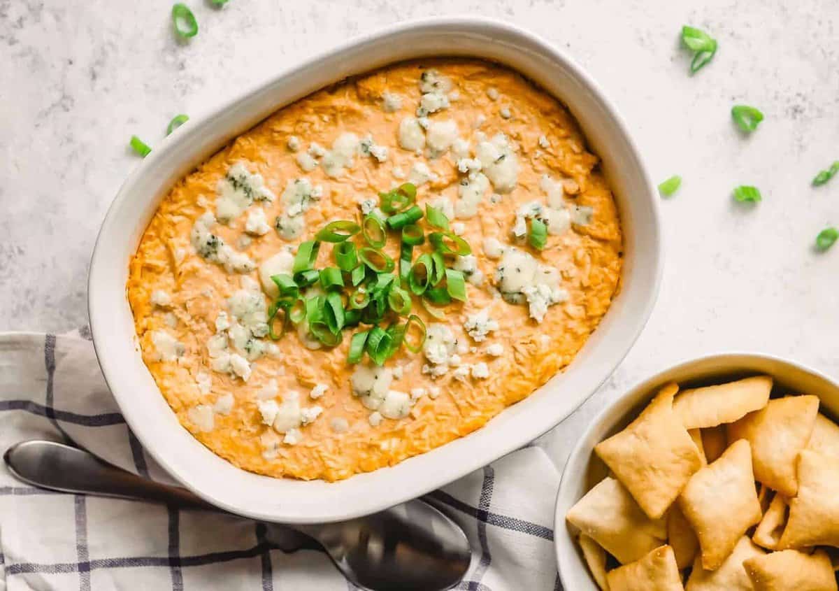 Buffalo Chicken Dip in a white dish topped with blue cheese and scallions