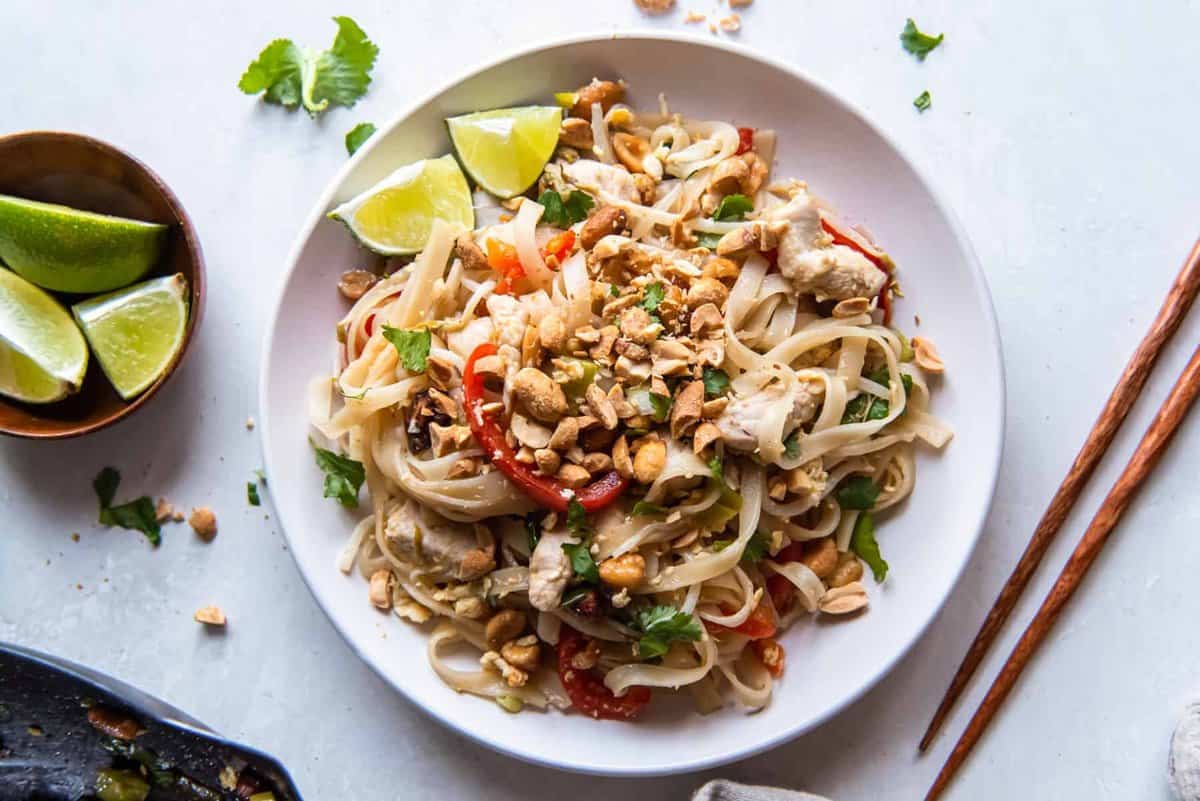 chicken pad thai on a white plate with chopsticks.