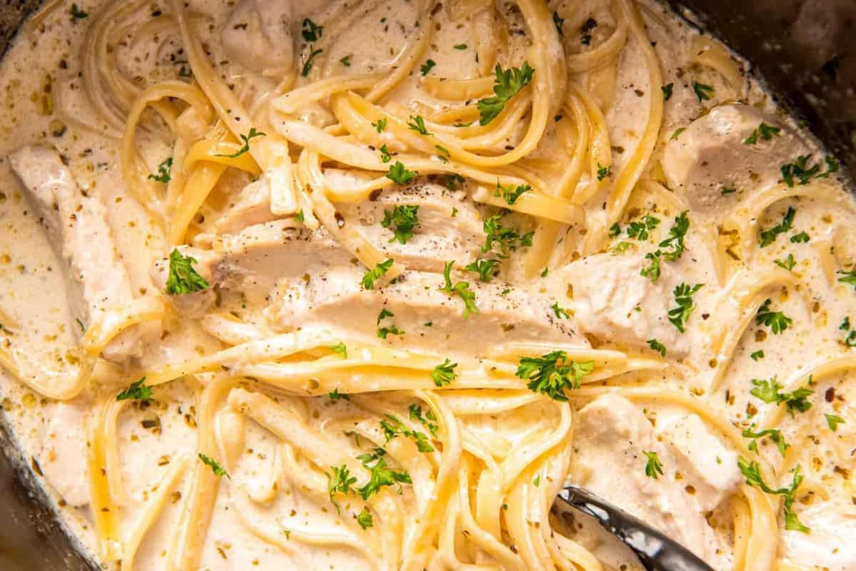close up of crockpot chicken alfredo with tongs.