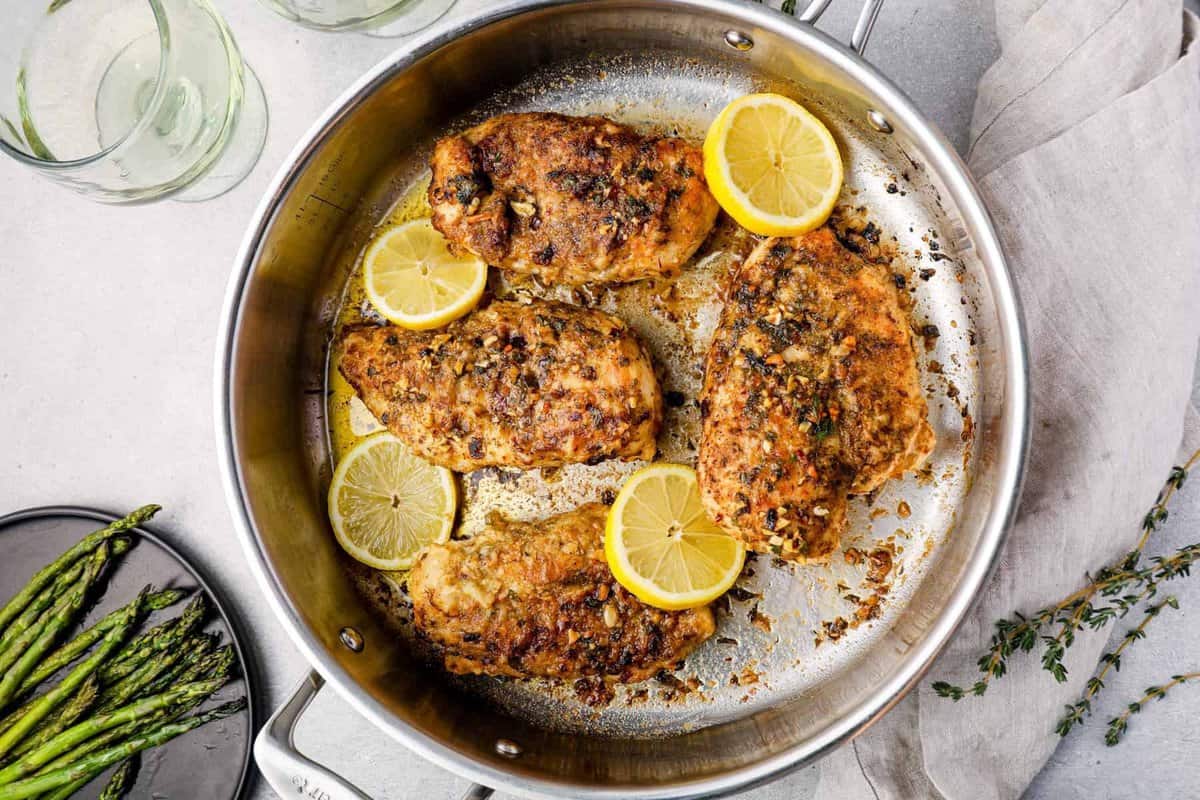 overhead view of garlic butter chicken and lemons cooking in a skillet
