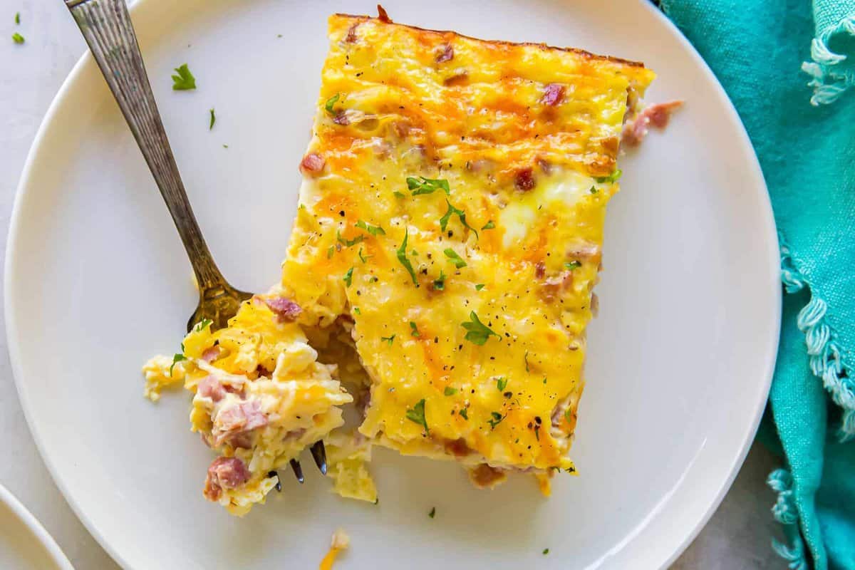 a forkful of ham and cheese breakfast casserole on a white plate.