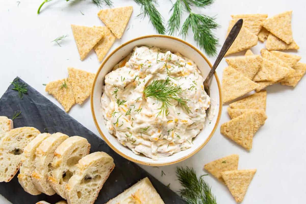 a bowl of ranch chicken dip on a table, with crackers and slices of bread next to it