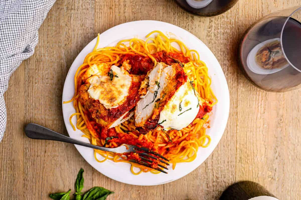 sliced stuffed chicken parmesan over pasta on a white plate with a fork.