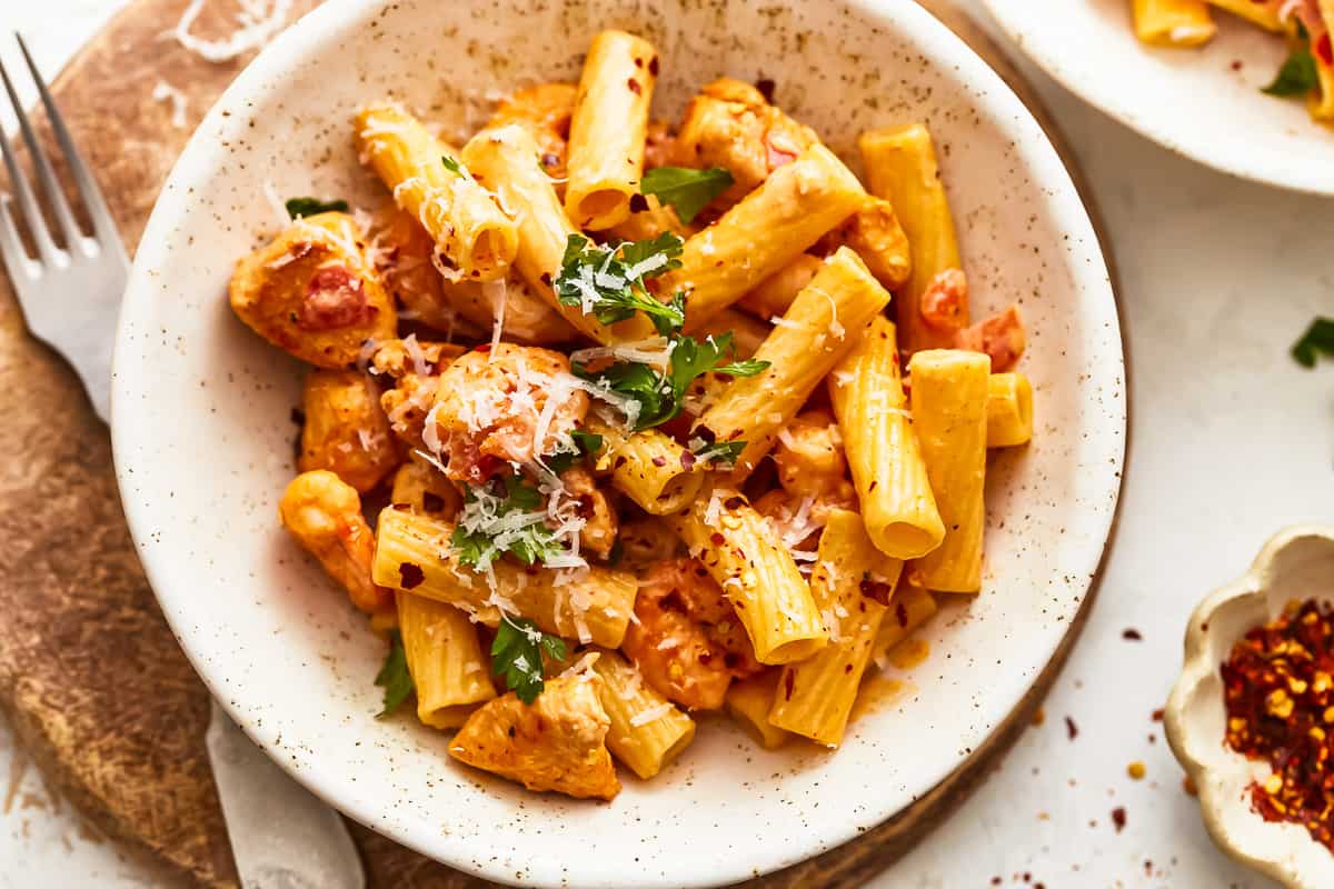 overhead view of a serving of cajun chicken pasta in a white bowl topped with cheese and parsley.