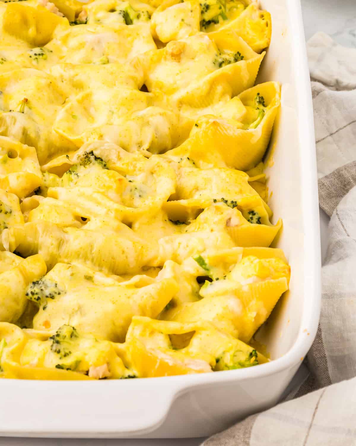 close up view of chicken and broccoli stuffed shells in a white casserole dish.