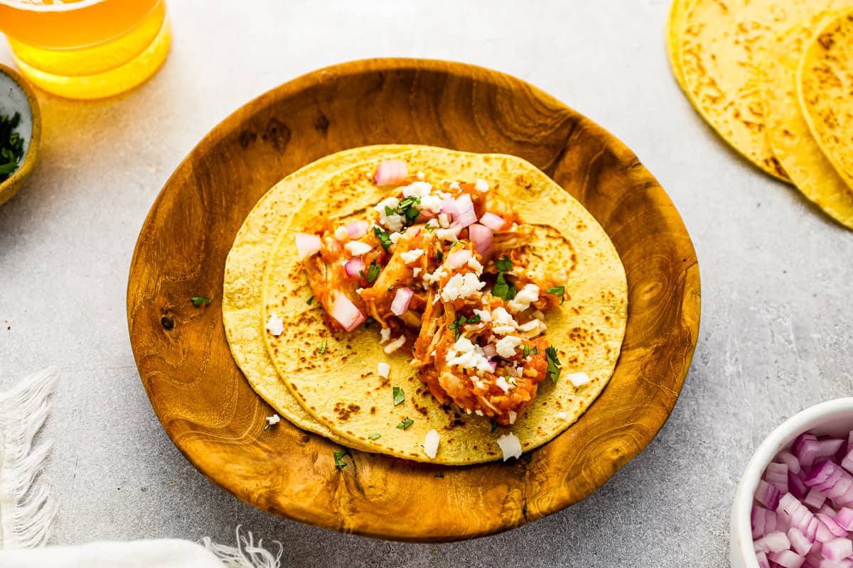 open-faced chicken tinga taco on a wooden plate.