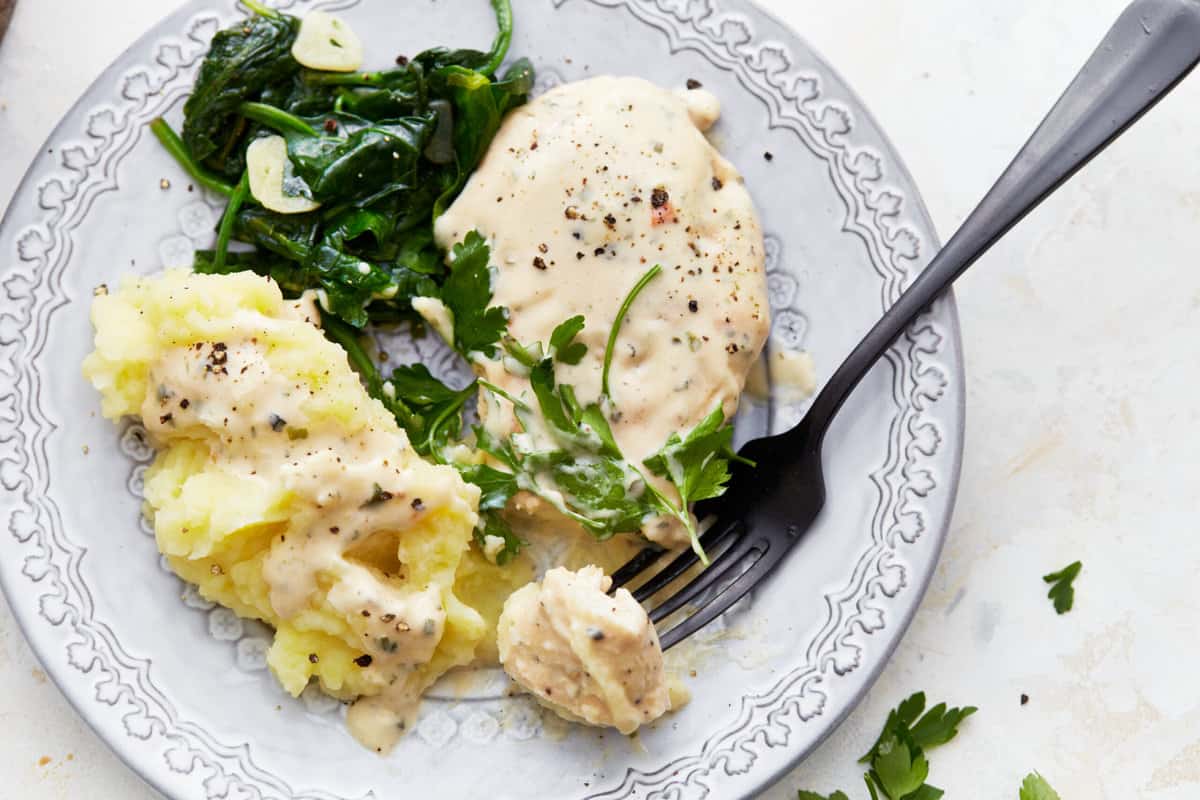 a serving of boursin chicken on a plate with spinach, mashed potatoes, and a fork.