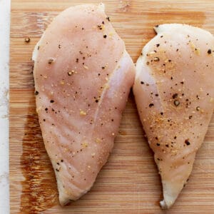 seasoned raw chicken breasts on a wood cutting board.