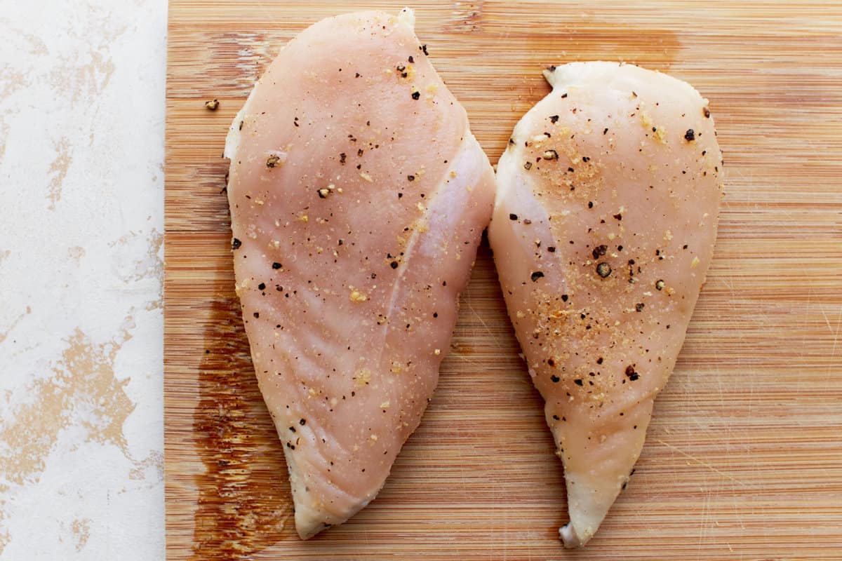 seasoned raw chicken breasts on a wood cutting board.