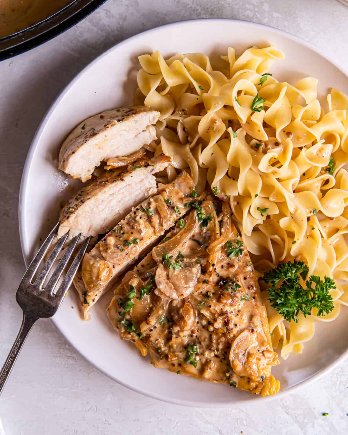 overhead view of a partially-sliced serving of chicken dijon with egg noodles on a white plate.