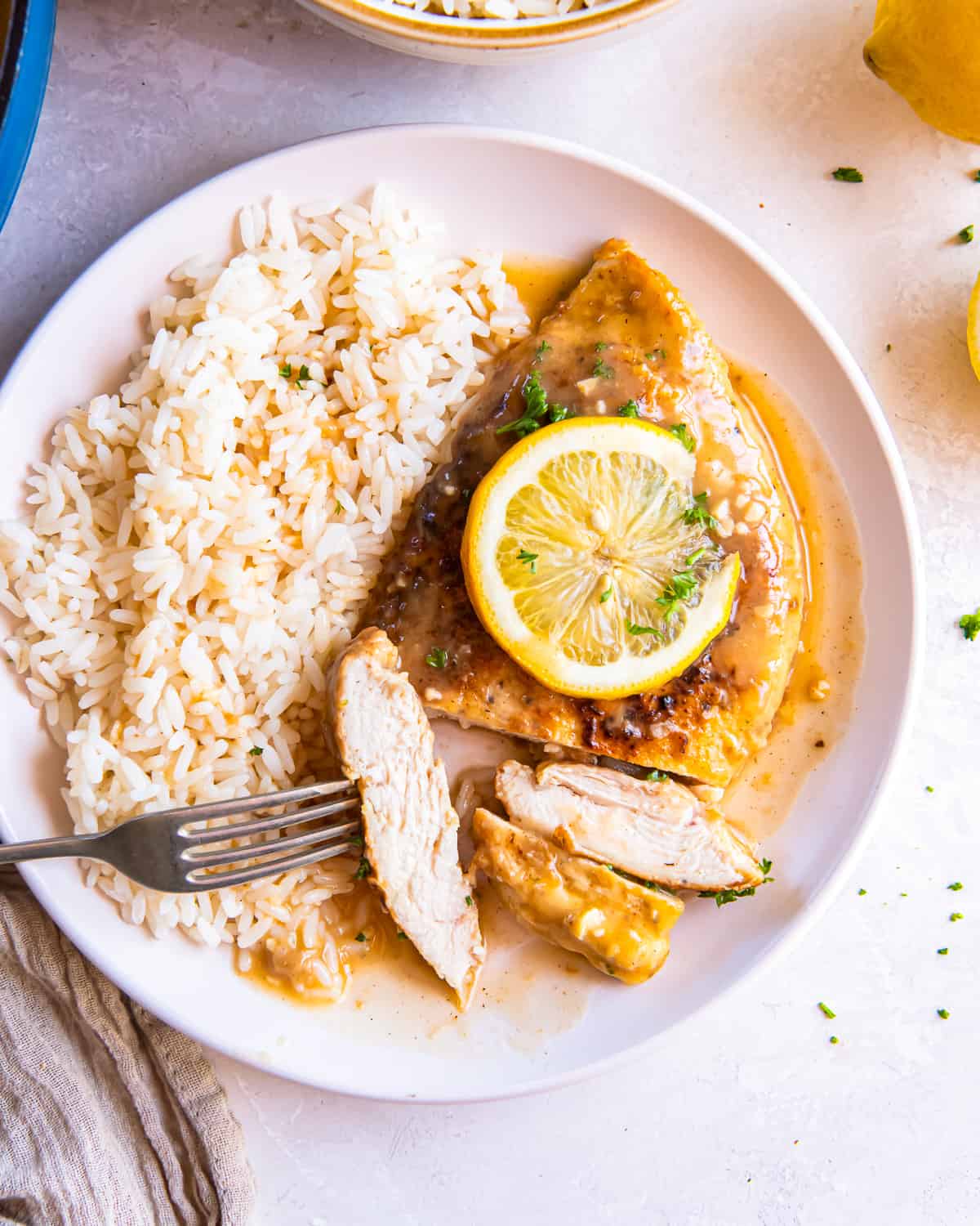 overhead view of a partially-sliced serving of chicken francese with rice on a white plate.