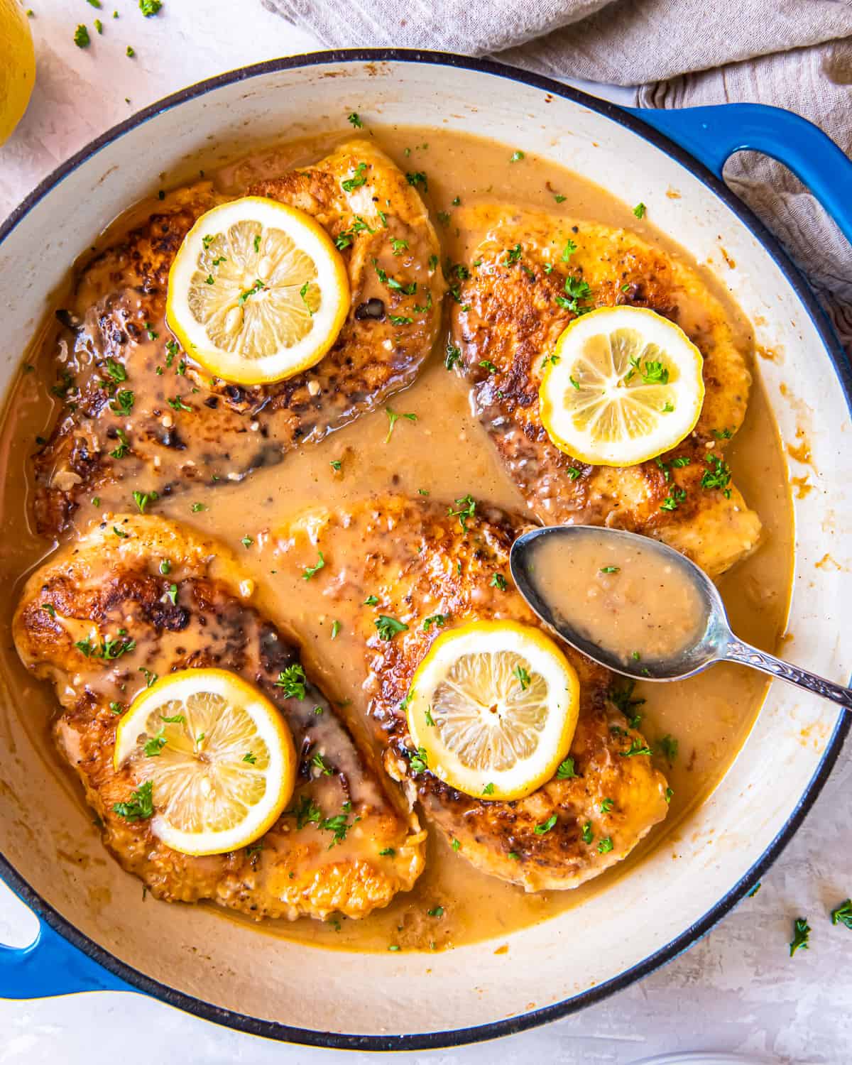 overhead view of chicken francese in a pan with a spoon.