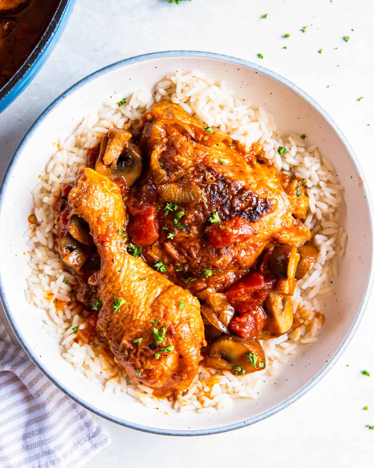 overhead view of a serving of chicken marengo over rice in a white bowl.