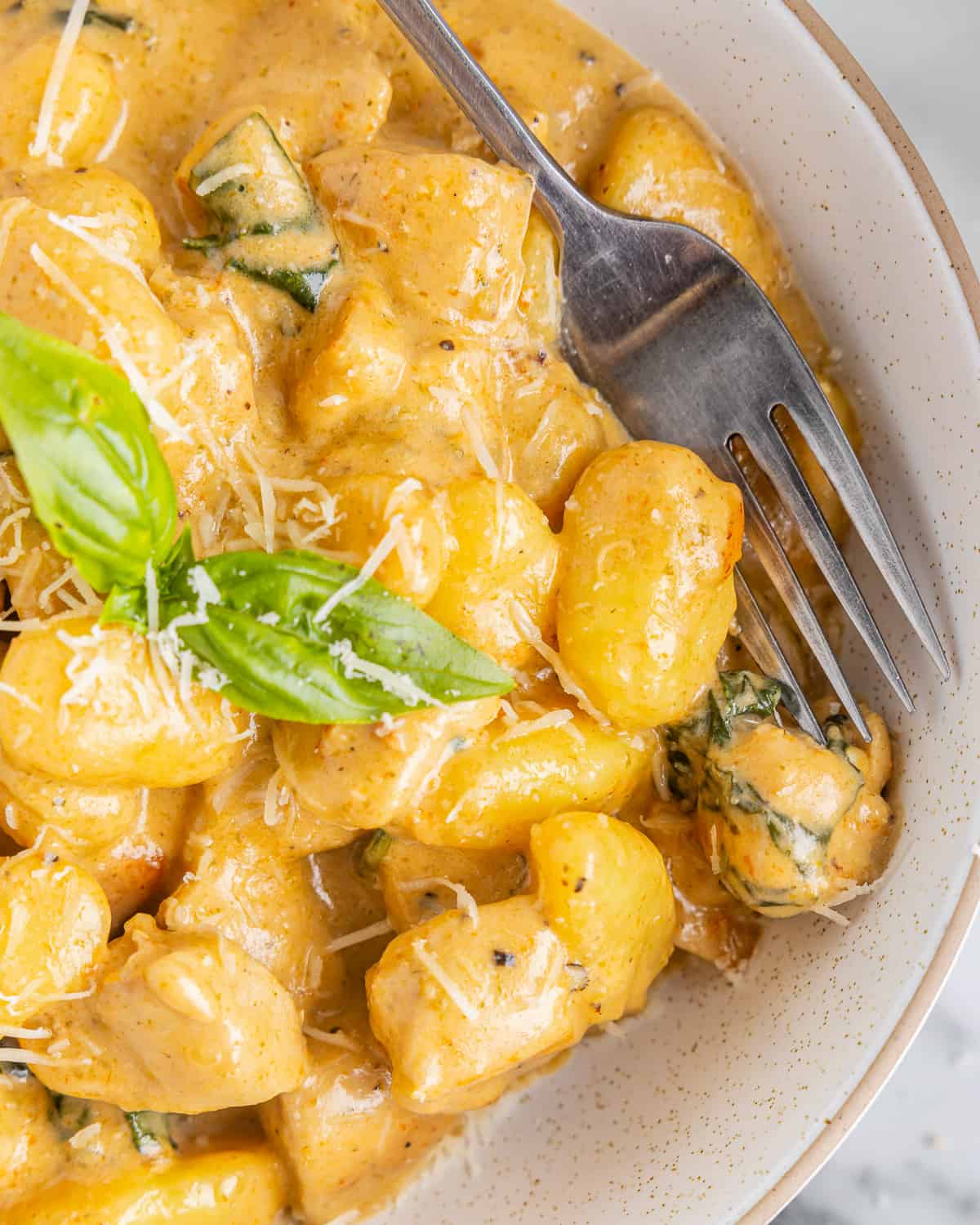 close up of creamy chicken gnocchi in a bowl with a fork.