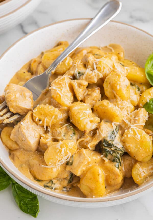 three-quarters view of creamy chicken gnocchi in a bowl with a fork.
