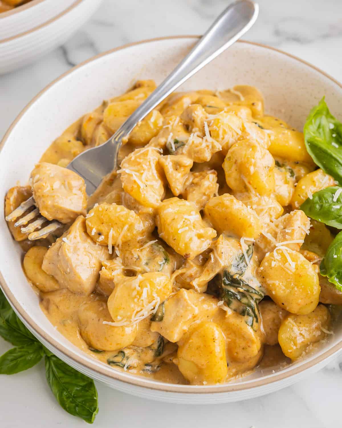 three-quarters view of creamy chicken gnocchi in a bowl with a fork.