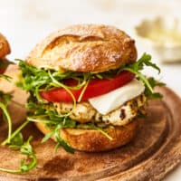 a pesto chicken sandwich on a wooden cutting board.