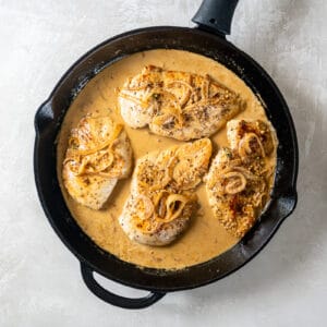 chicken breasts added to dijon mustard sauce in a cast iron pan.
