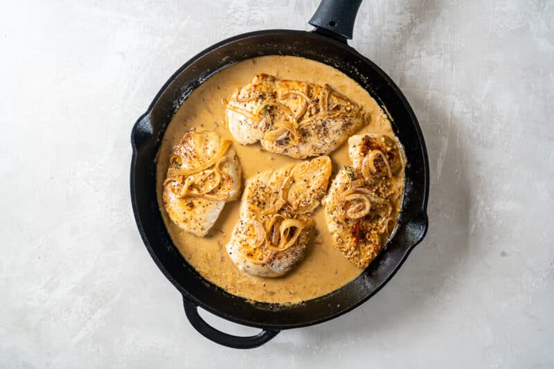 chicken breasts added to dijon mustard sauce in a cast iron pan.