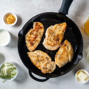 overhead view of 4 cooked chicken breasts in a cast iron pan.
