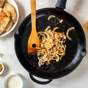 cooked sliced onion and garlic in a cast iron pan with a wooden spoon.