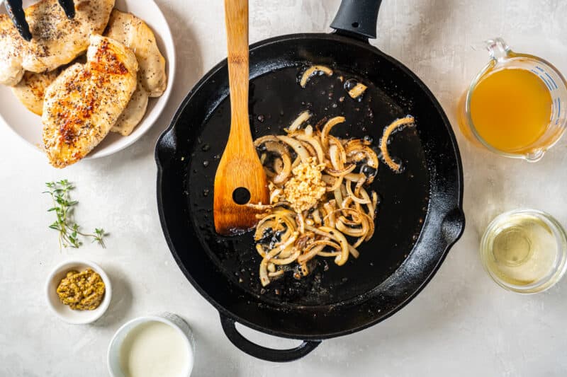 cooked sliced onion and garlic in a cast iron pan with a wooden spoon.